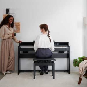 Lehrerin steht neben Schülerin, welche am Casio AP-S450 E-Piano übt